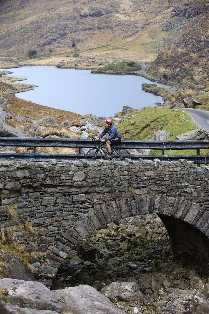 A cyclist rides across a stone bridge overlooking a lake in the Gap of Dunloe on the Ring of Kerry.