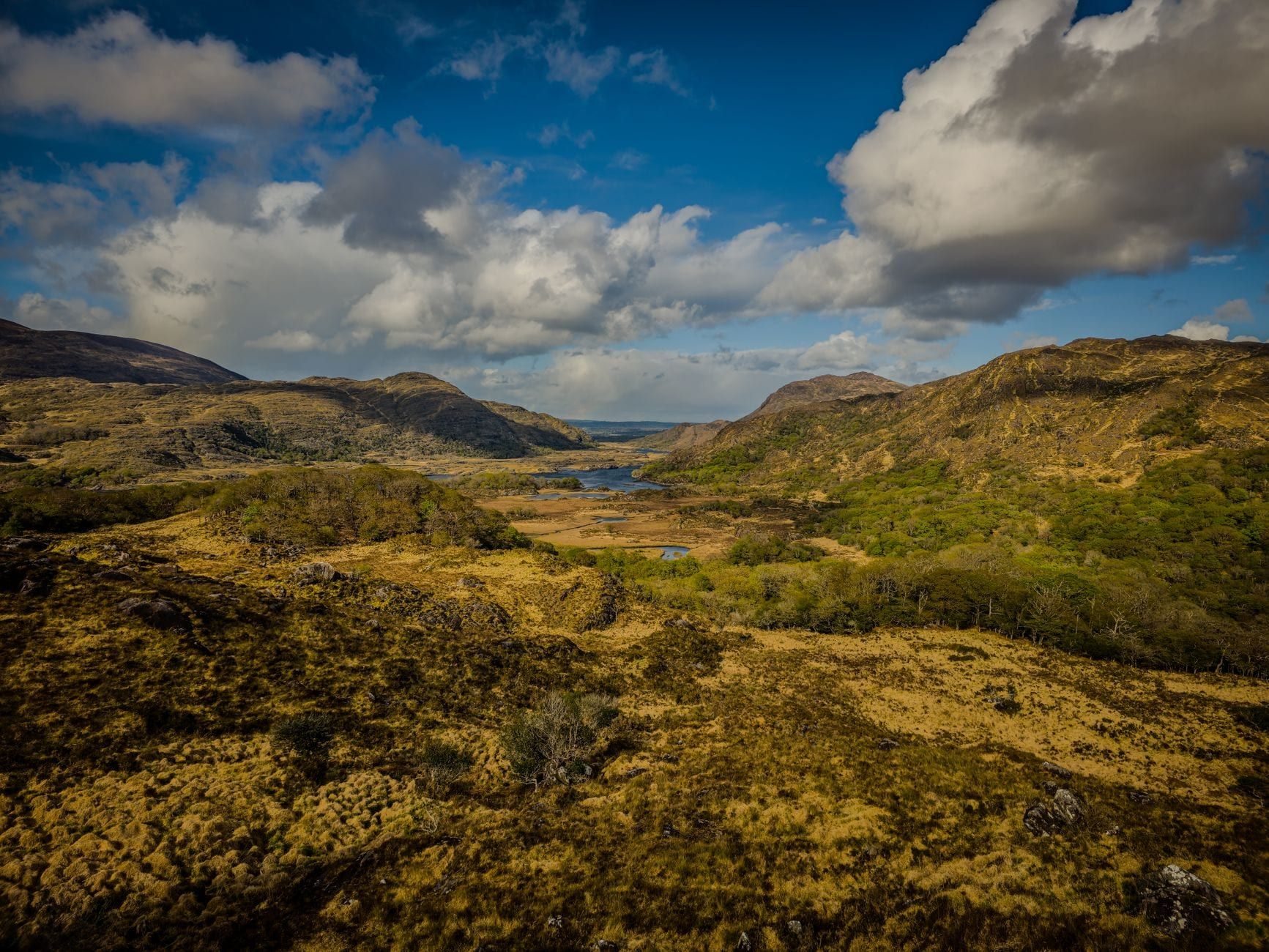 Panoramablick auf schroffe Berge und Seetäler vom Ladies View entlang des Ring of Kerry unter teils bewölktem Himmel.