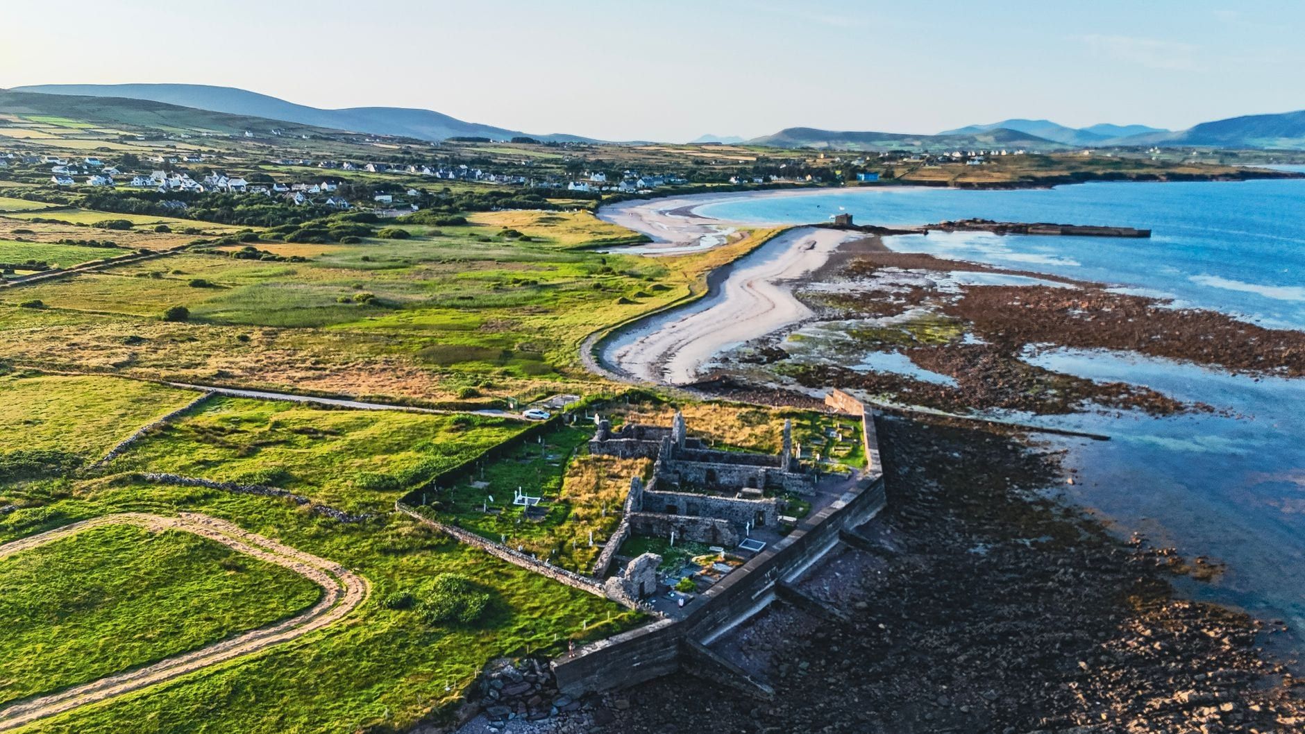 Luftaufnahme der Küstenruinen der Ballinskelligs Abbey und des sandigen Ufers entlang des Ring of Kerry in County Kerry.