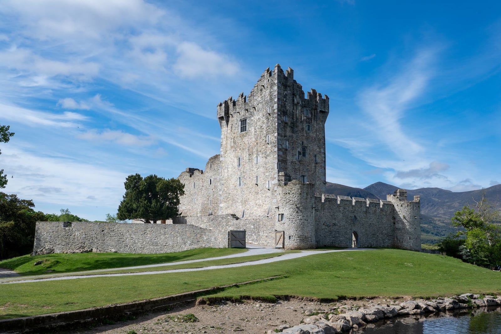 Stone tower house and curtain walls of Ross Castle stand on a grassy knoll in Killarney National Park near the Ring of Kerry.