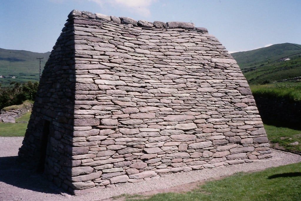 Ancient dry-stone corbelled structure of Gallarus Oratory set against the rolling green hills of the Dingle Peninsula in County Kerry.